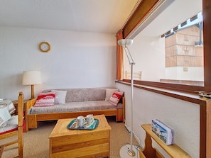 Una habitación acogedora con un sofá, una mesita de madera con una bandeja, una lámpara y una ventana con vistas a edificios.