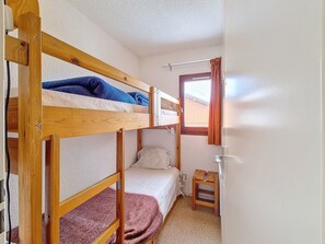 Habitación con literas, una ventana, un taburete de madera y un radiador.