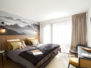 A hotel room with a bed, a desk, and a view of mountains through the window. - Bright apartment 75sqm, calm, near slopes - 6 guests (Les Deux Alpes)