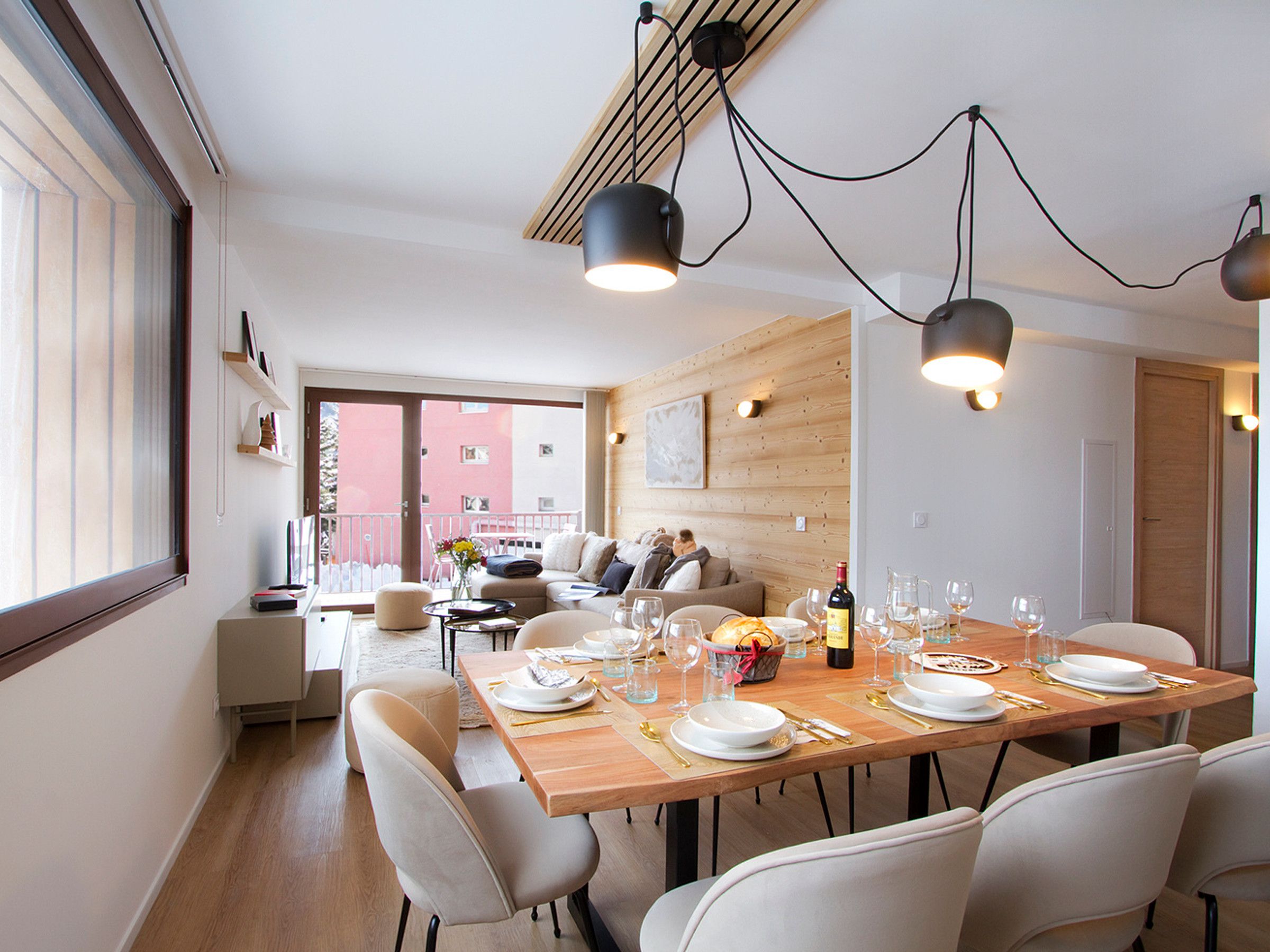 Een eetgedeelte met een houten tafel gedekt voor een maaltijd, een bank en uitzicht op een gebouw.