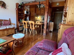 A cozy living room with a wooden sofa, a dining table with chairs, and a kitchen area with wooden cabinets. - Apartment, pets OK - mountain view (4 guests) (Samoëns)