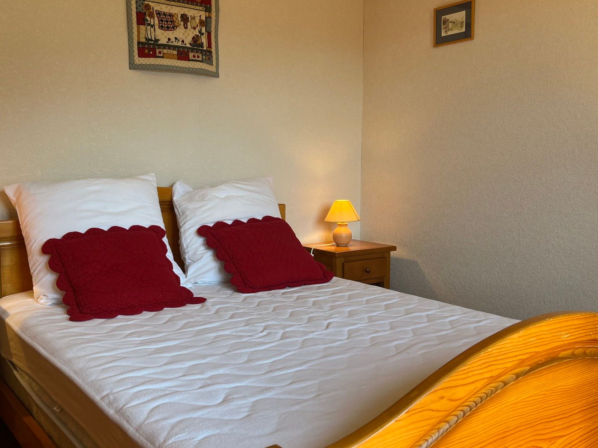 A bed with white bedding and two red pillows, a bedside lamp, and a small table with a lamp.