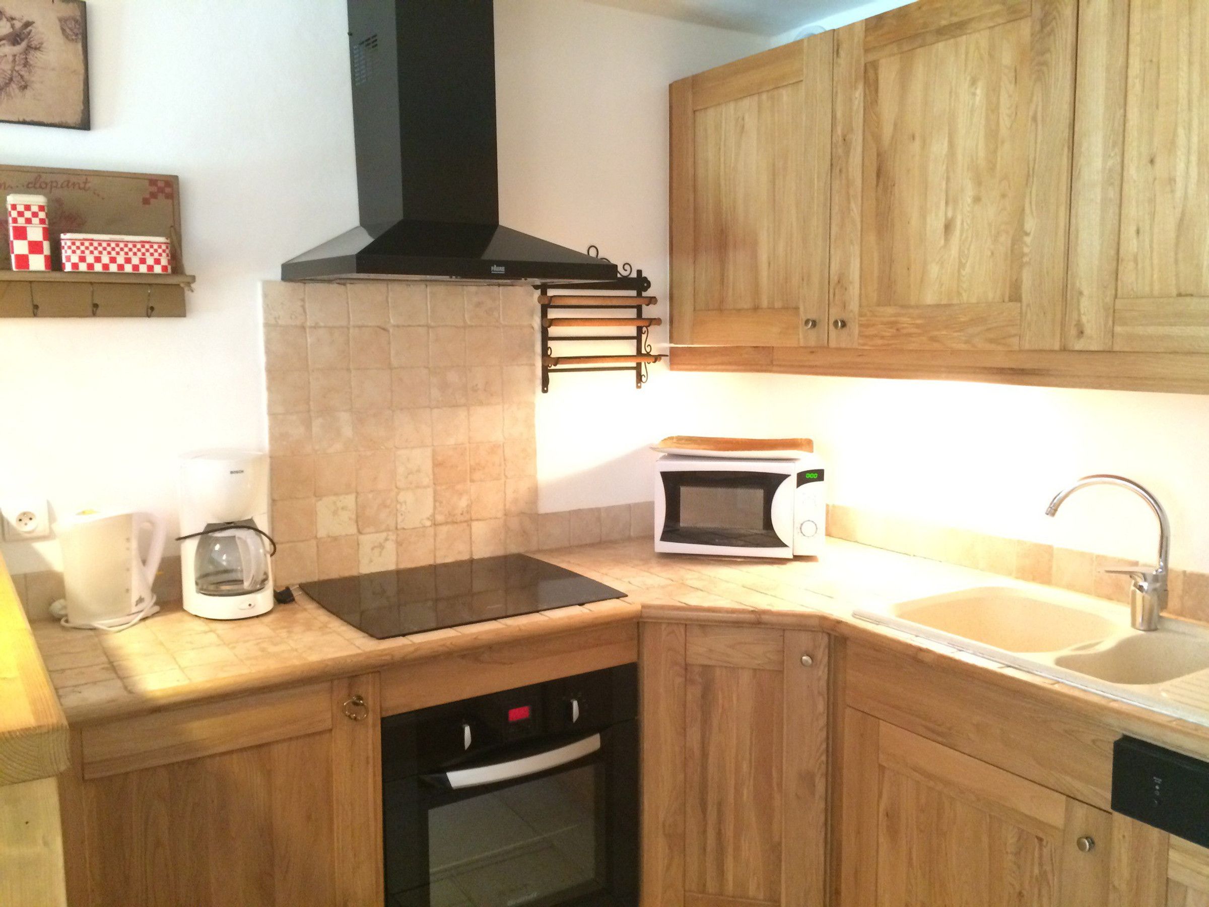 A kitchen with wooden cabinets, a black range hood, a microwave, a coffee maker, and a dishwasher.