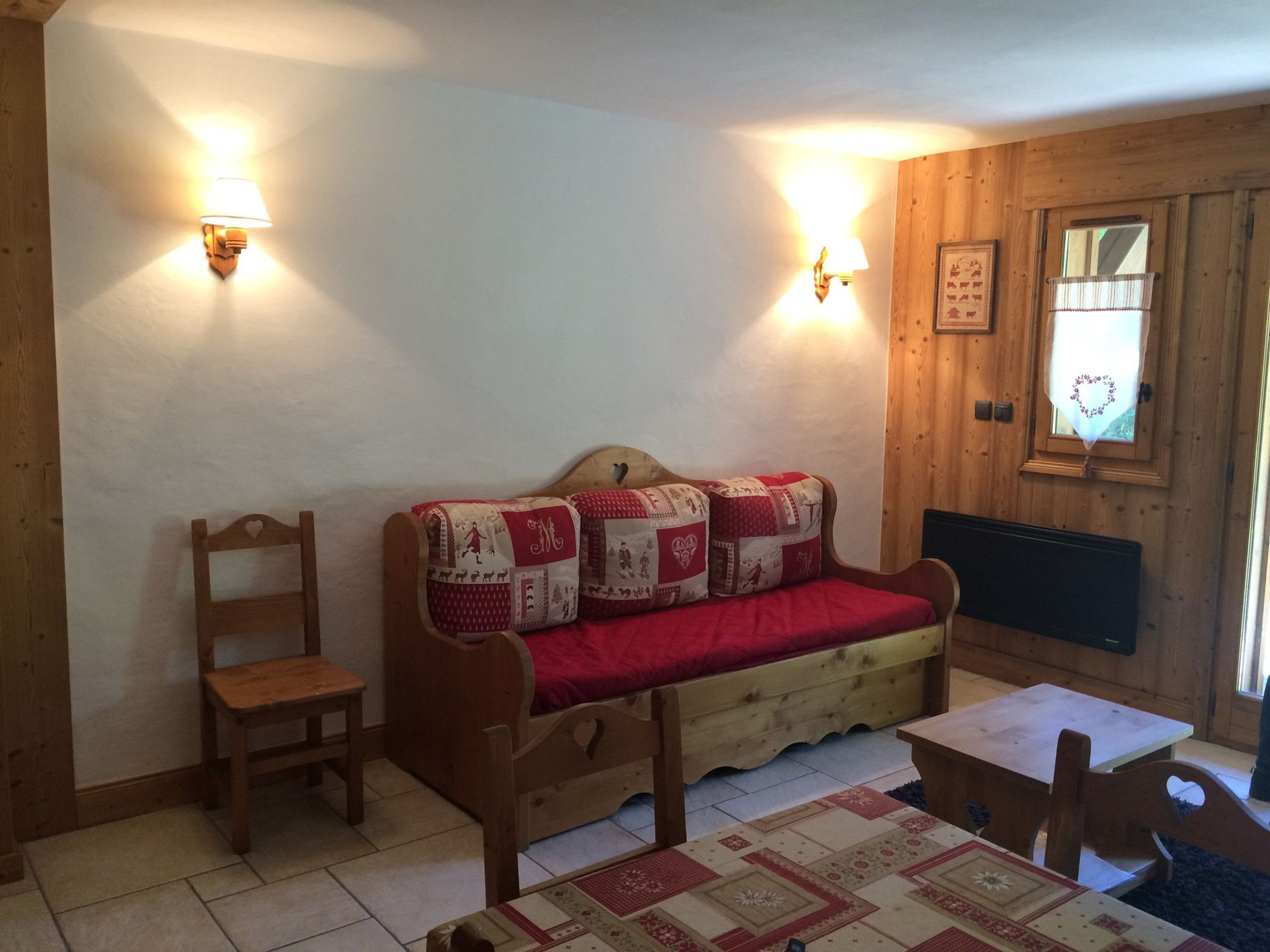 A cozy room with a wooden sofa, a small wooden table, and a wall-mounted light fixture.
