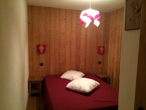 Un dormitori amb una paret de fusta, dues taules de nit, un llit amb roba de llit blanca i una làmpada penjant.