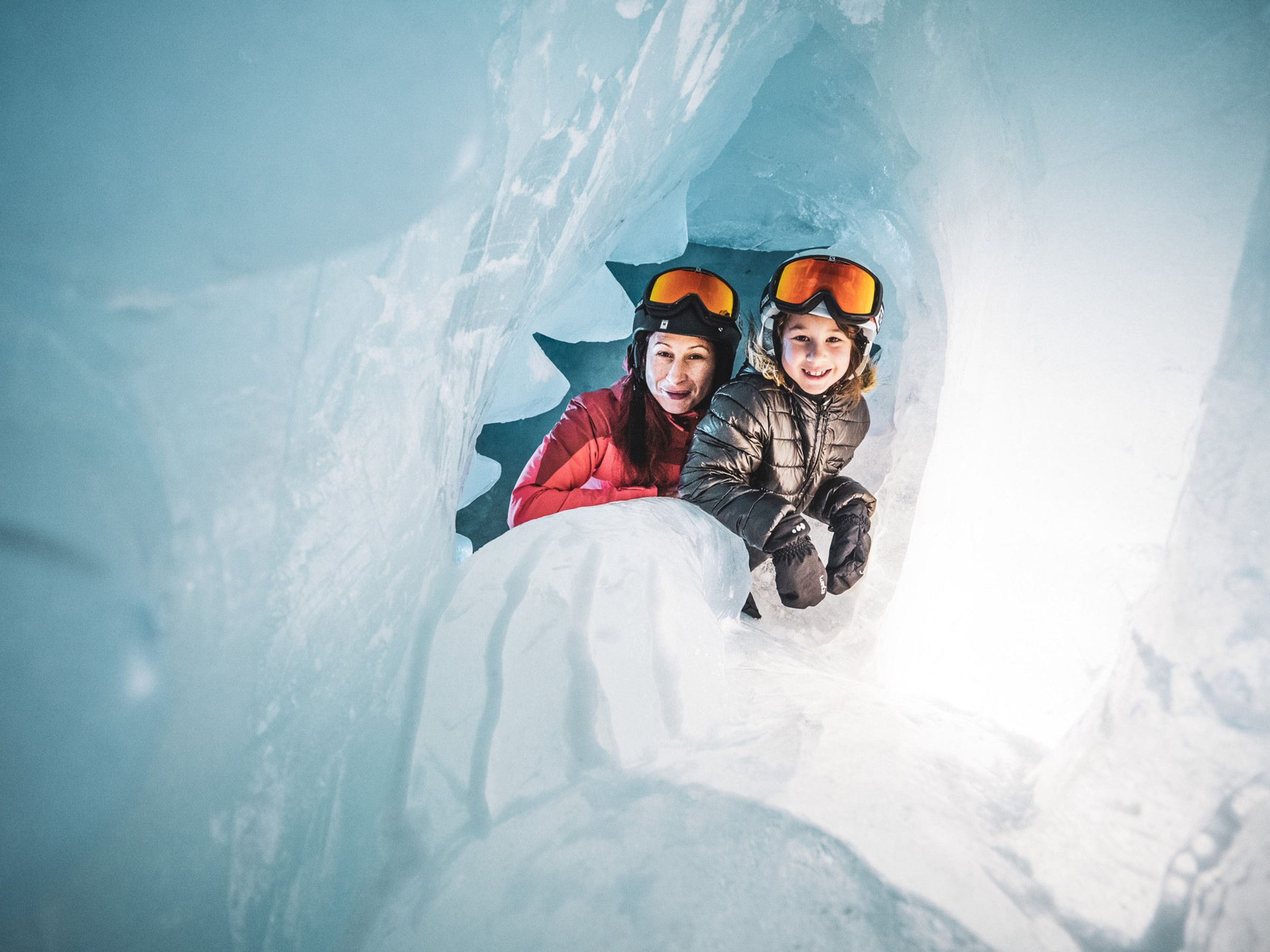 Two individuals inside an ice cave with snow-covered walls.