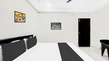 Un dormitorio con una cama, un ventilador de techo, una puerta y dos cuadros en la pared.