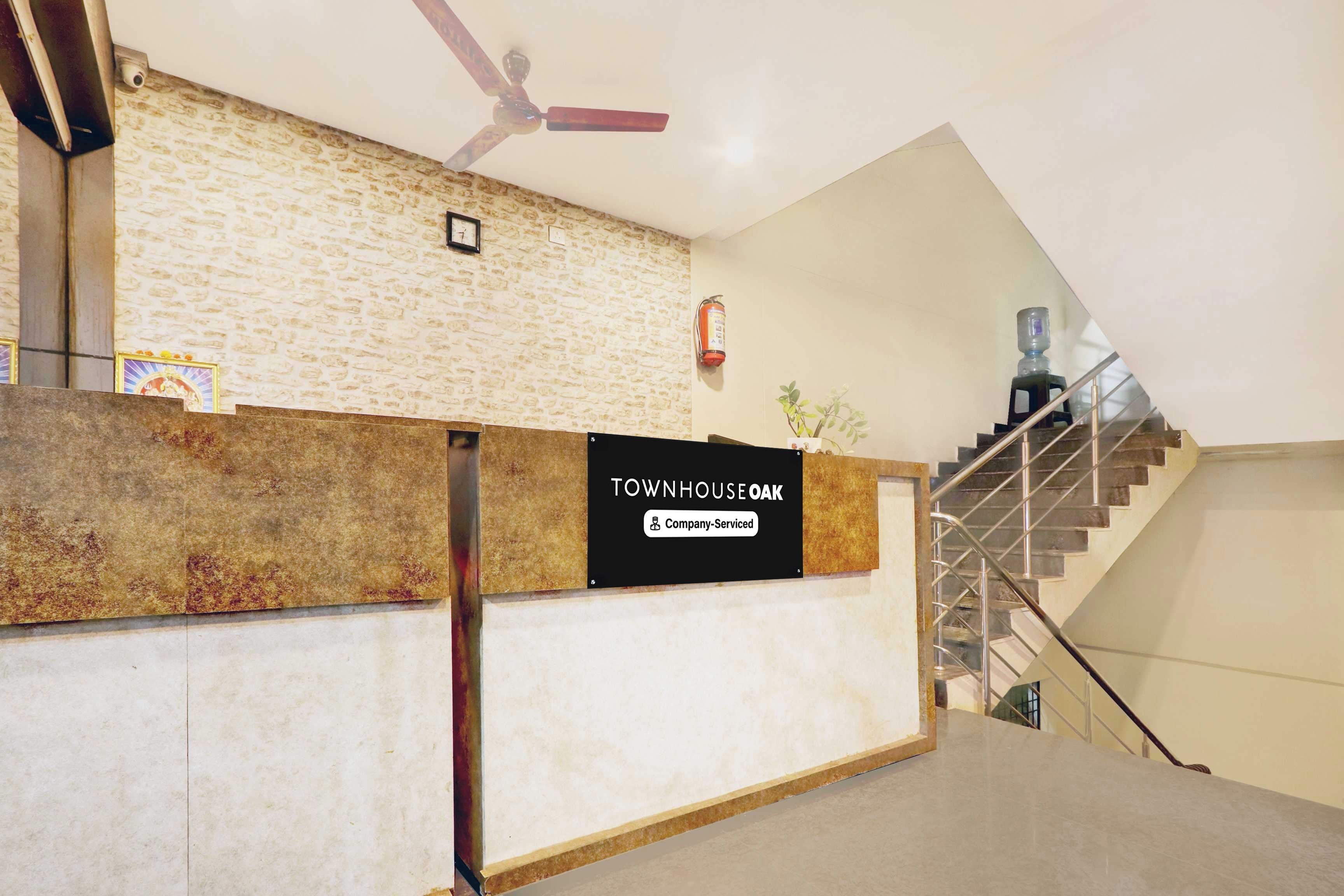 A reception desk with a sign indicating it is company-serviced, a fire extinguisher, a ceiling fan, and a staircase with metal railings.
