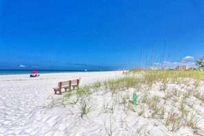 A sandy beach with a wooden bench and a red umbrella. - Beachfront Condo | Heated Pool | Private Balcony - Gulf Shores #404 (Indian Shores)