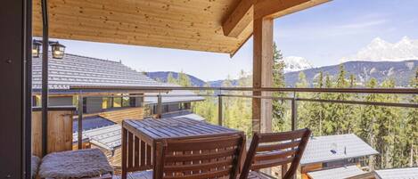 Una terraza de madera con mesa y sillas, con vistas a un paisaje montañoso.