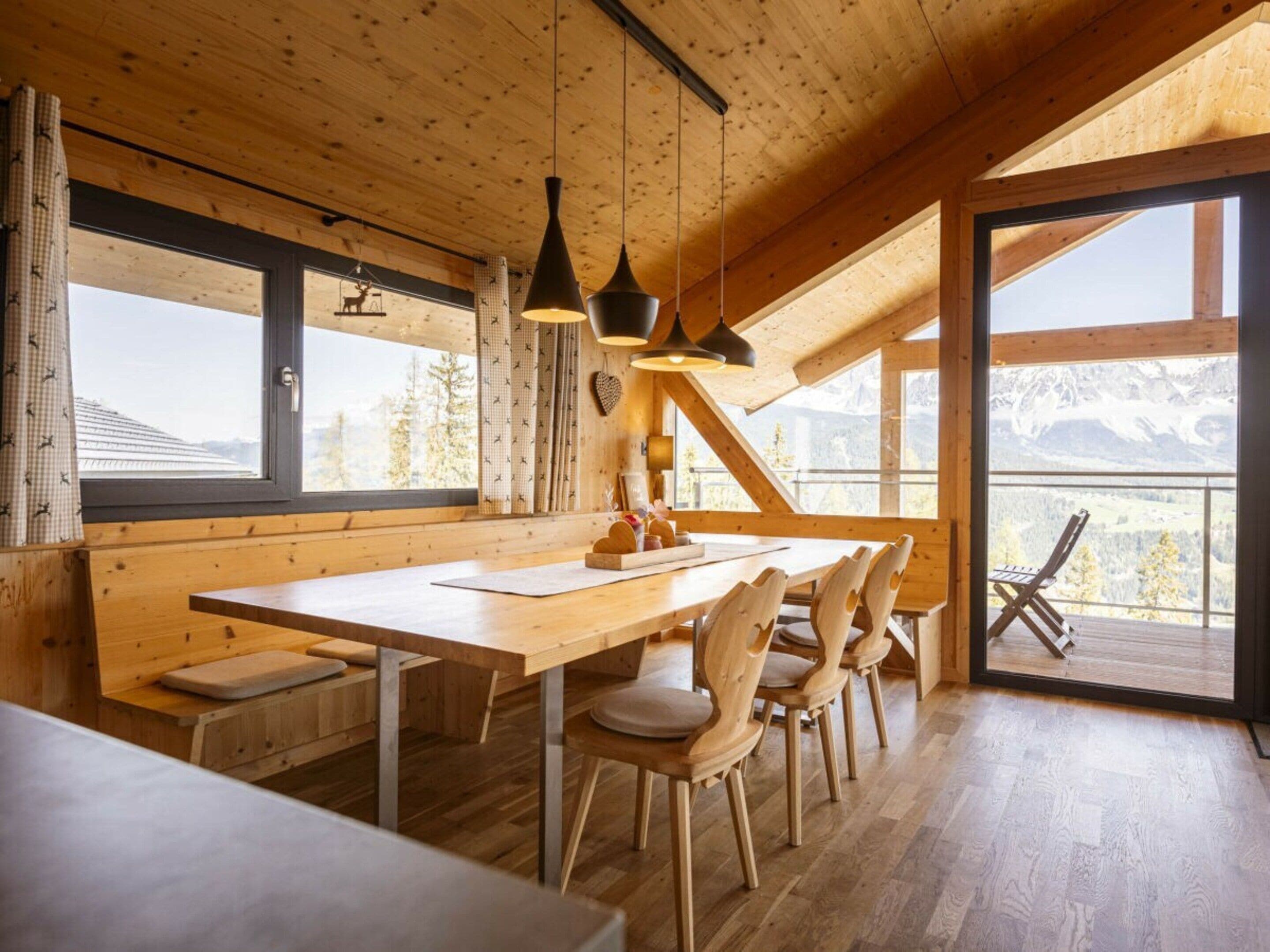 Un interior de madera con comedor, ventanas amplias y vistas a montañas.
