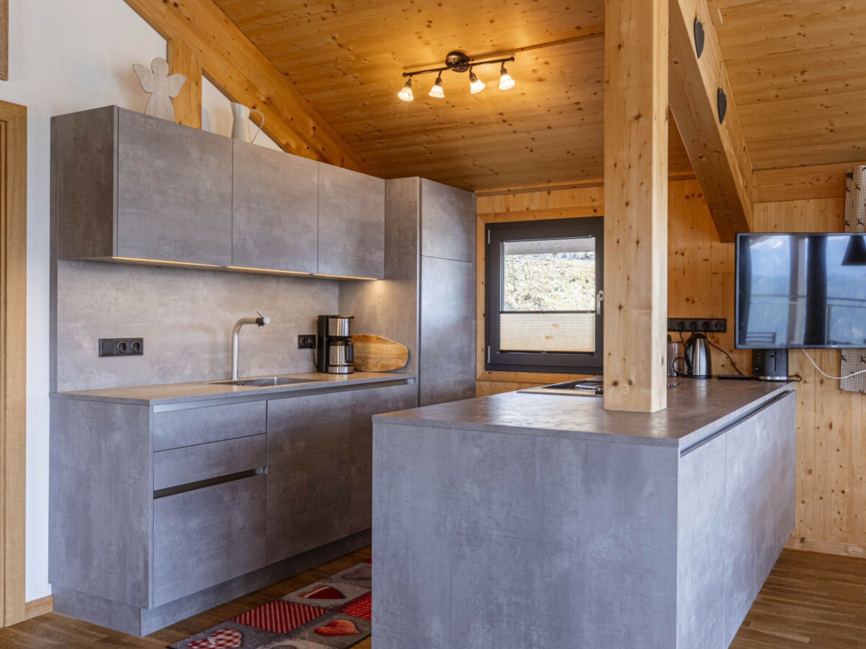 Une cuisine moderne avec des meubles gris, une cuisinière encastrée et une grande fenêtre.