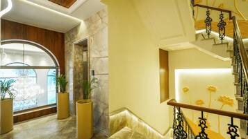 A modern interior with a marble floor, a wooden ceiling, a staircase with black railings, and potted plants.
