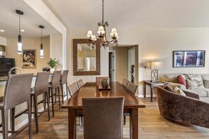 A dining area with a large wooden table, multiple chairs, a chandelier, and a sofa. - Ski-In/Ski-Out Beaver Creek | UB205 (Avon)