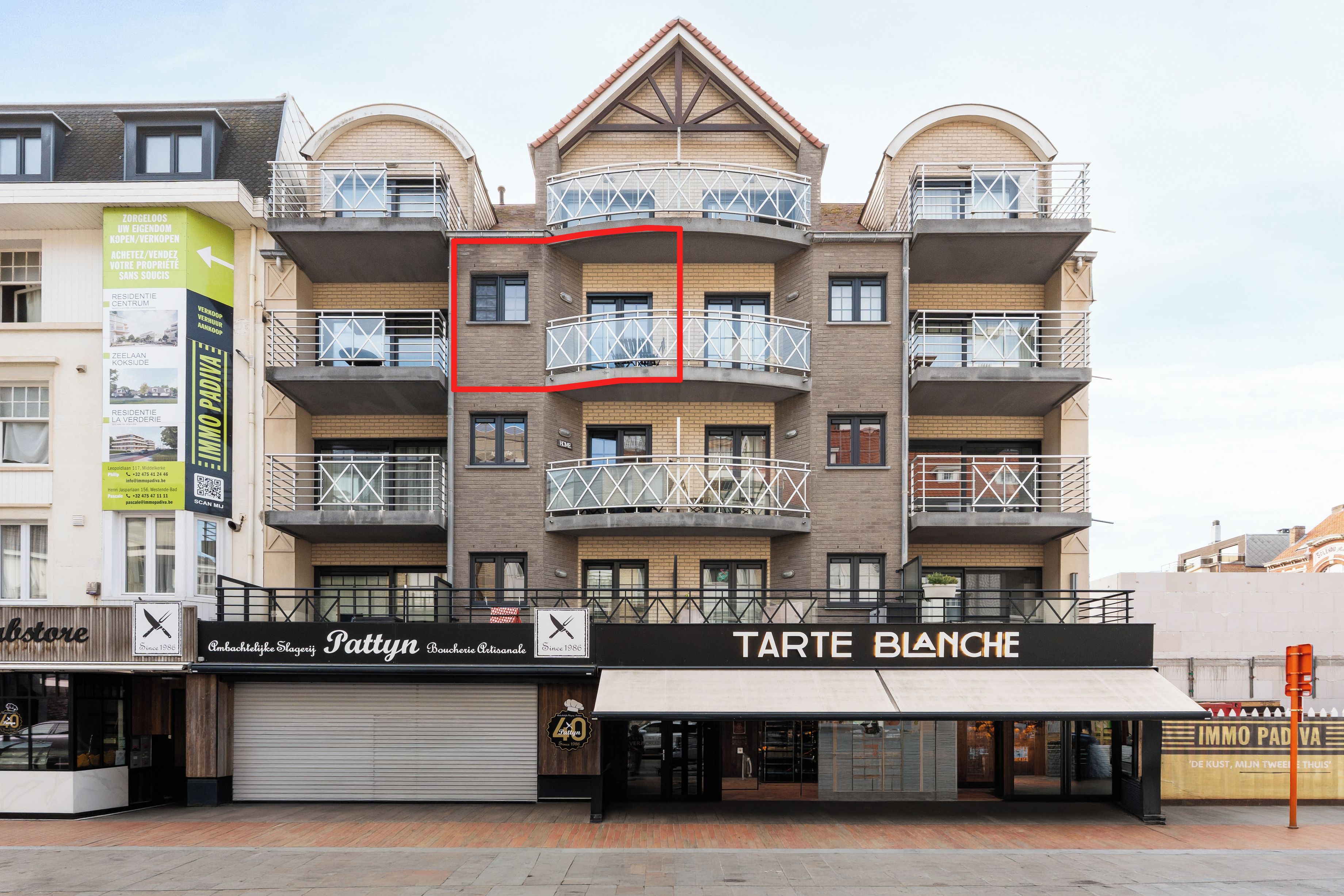 Een meerlaags gebouw met balkons, een winkel met een bordje 'Tarte Blanche' en een bord dat 'Zorgeloos' adverteert.