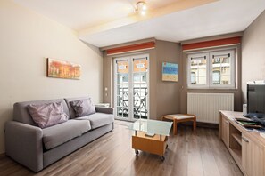 Ein modernes Wohnzimmer mit einem grauen Sofa, einem Glastisch und einem Holzschrank mit einem Laptop.