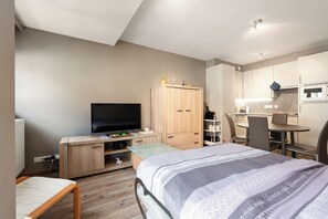 Une chambre compacte comprenant un lit, une télévision, un bureau et une kitchenette.
