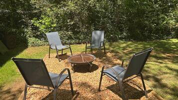 Un espace extérieur aménagé avec quatre chaises en métal et une table ronde, entouré de gravier et de verdure.