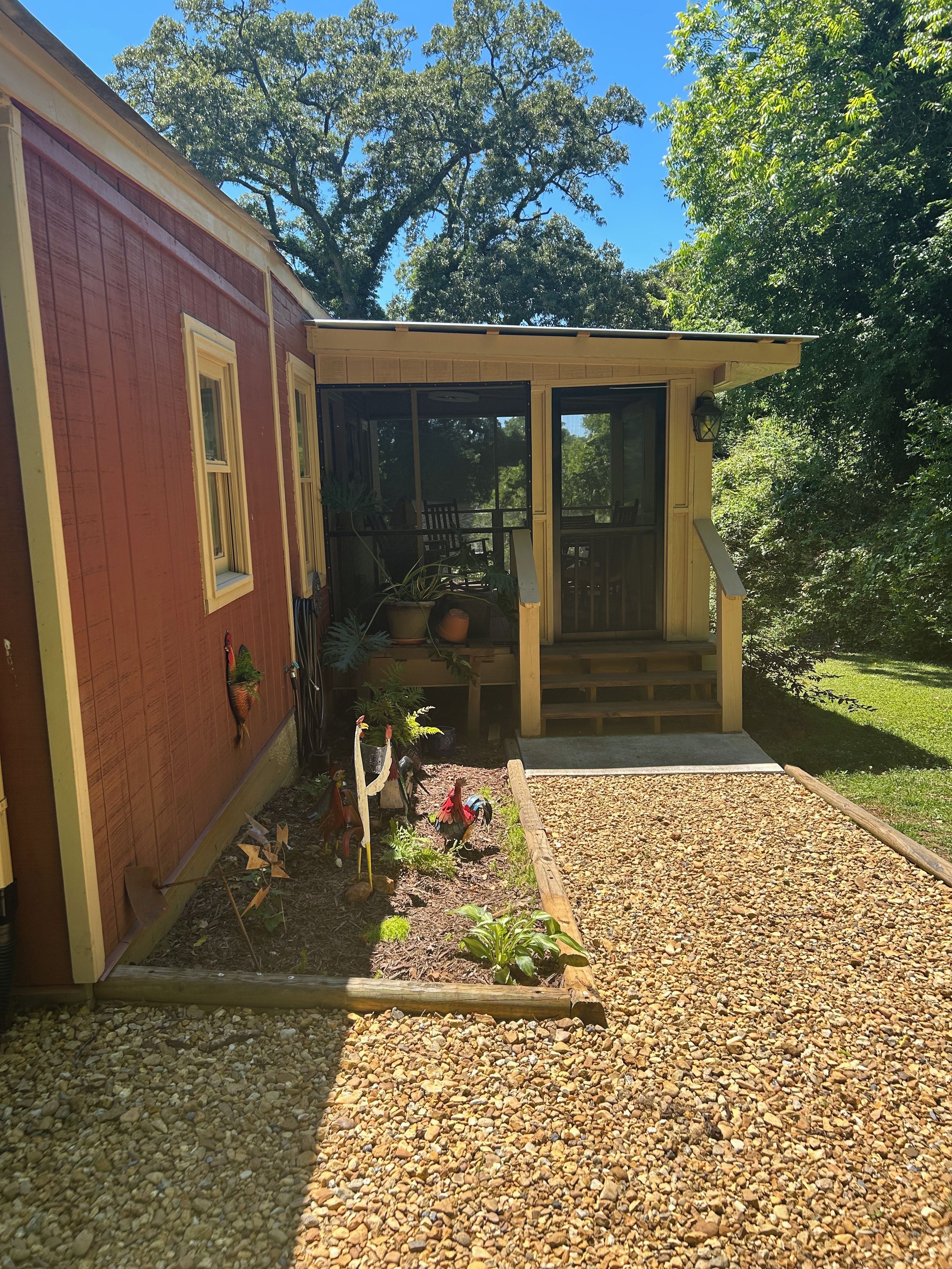 Ein Haus mit überdachter Veranda, einem Schotterweg und einem Garten mit Pflanzen und einem Vogelhäuschen.