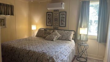 Quarto com cama, duas luminárias fixadas na parede, aparelho de ar condicionado e janela com cortinas.