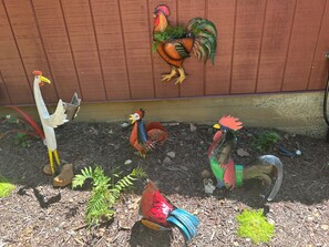 A garden with decorative chickens and a painted rooster on a wooden wall.