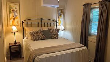 A neatly made bed with patterned pillows, a bedside lamp, a small nightstand, and a wall-mounted air conditioner.