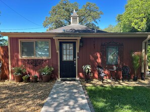A house with a front door, two windows, a chimney, and a small porch with potted plants.