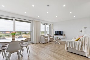 A modern living room with a large TV, comfortable seating, and a view of the outdoors. - 2 bedroom accommodation in Middelkerke (Middelkerke)