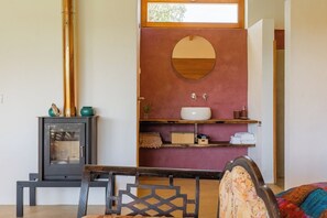 A room with a wood-burning stove, a mirror, and a shelf with toiletries.