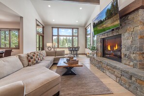 A spacious living room with a stone fireplace, a large window, and a cozy seating area. - Gray's Crossing Golf Estate 4 Bedroom Home (Truckee)