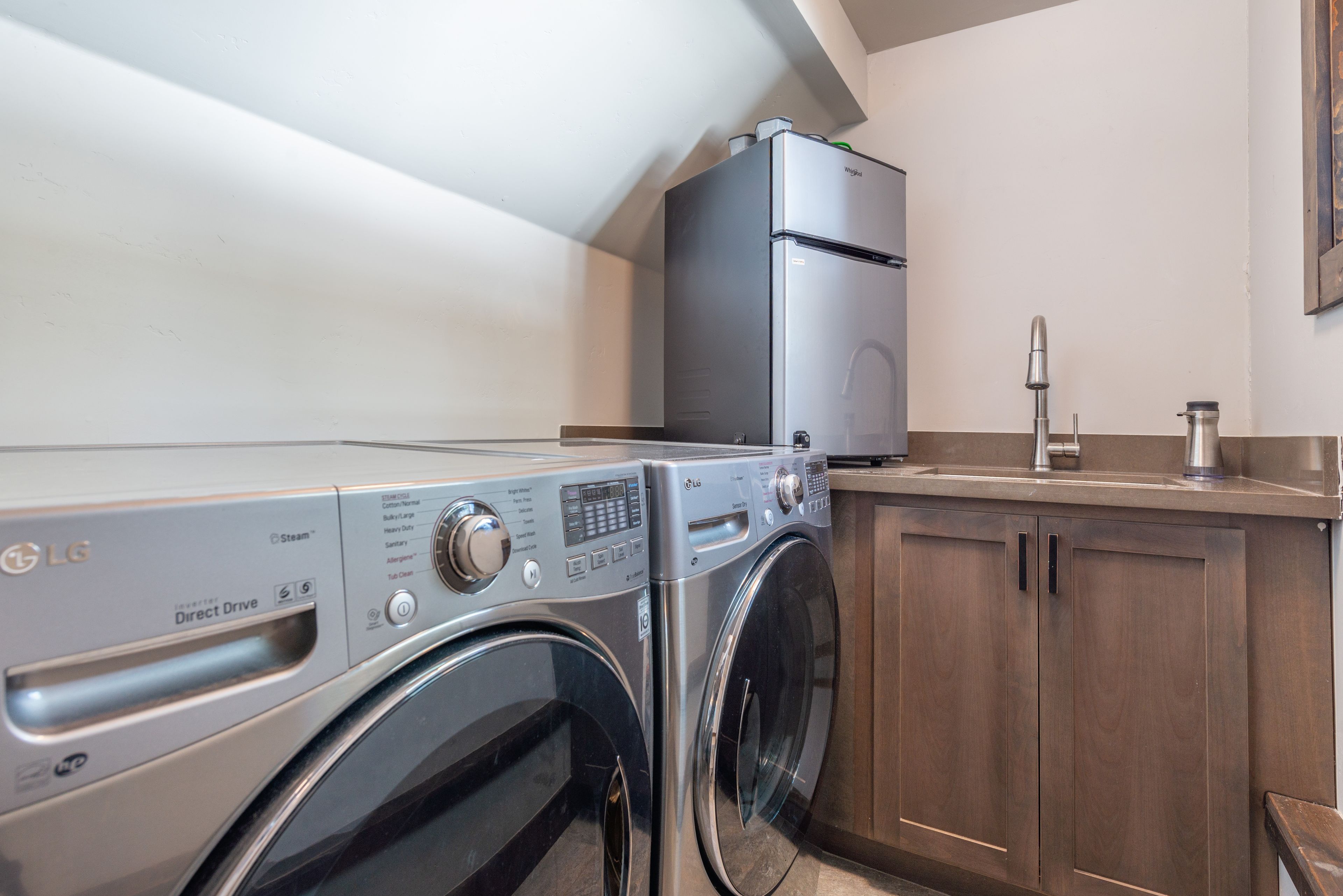 A laundry area with an LG washer and dryer, a Whirlpool refrigerator, and a wooden cabinet.