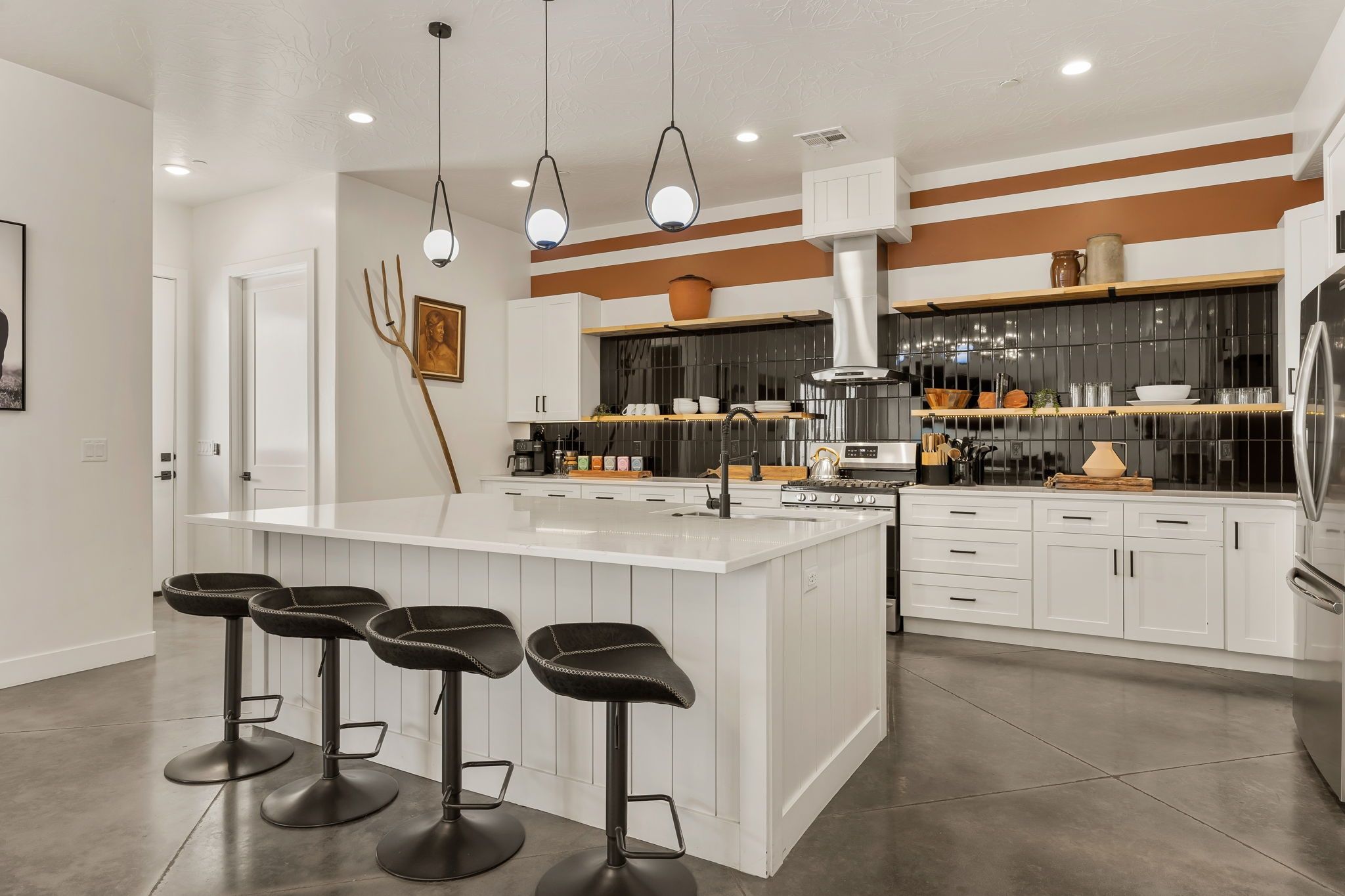 A modern kitchen with a central island, bar stools, and a stainless steel refrigerator.