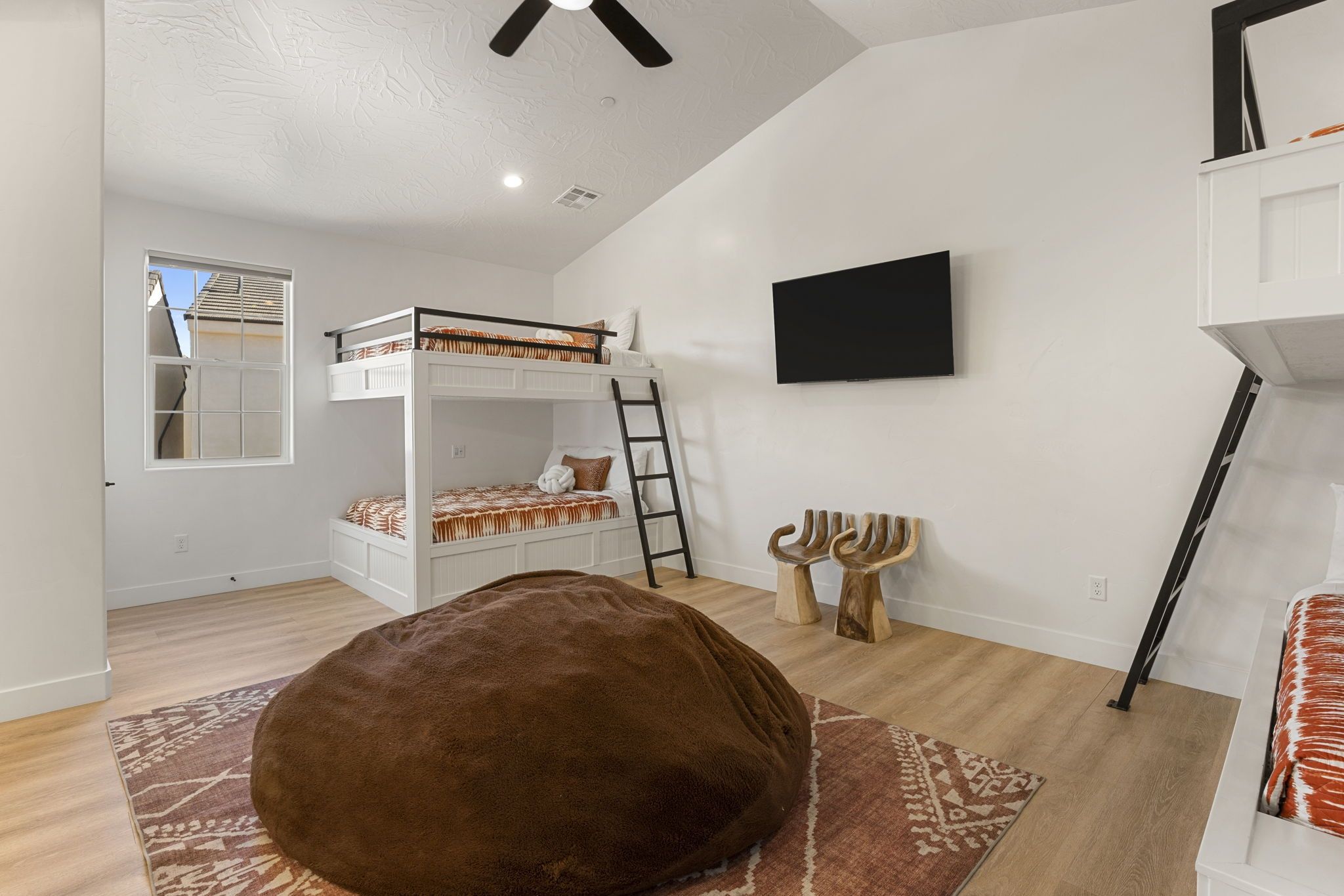 A room with a bunk bed, a large bean bag, a ladder, and a mounted TV.