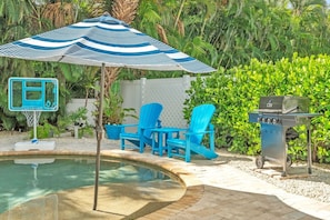 A pool area with a blue and white striped umbrella, a basketball hoop, and a barbecue grill. - Blue Star Oasis 4 Bedroom Home (Holmes Beach)
