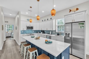 A modern kitchen with white cabinets, a stainless steel refrigerator, and a large island with stools. - Blue Star Oasis 4 Bedroom Home (Holmes Beach)