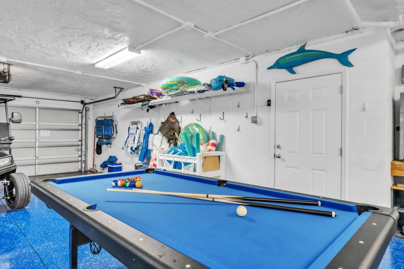 A pool table with balls, a car, and marine life decorations in a garage.