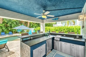 Cuina amb illa integrada, ventilador de sostre i vista a una piscina i vegetació.