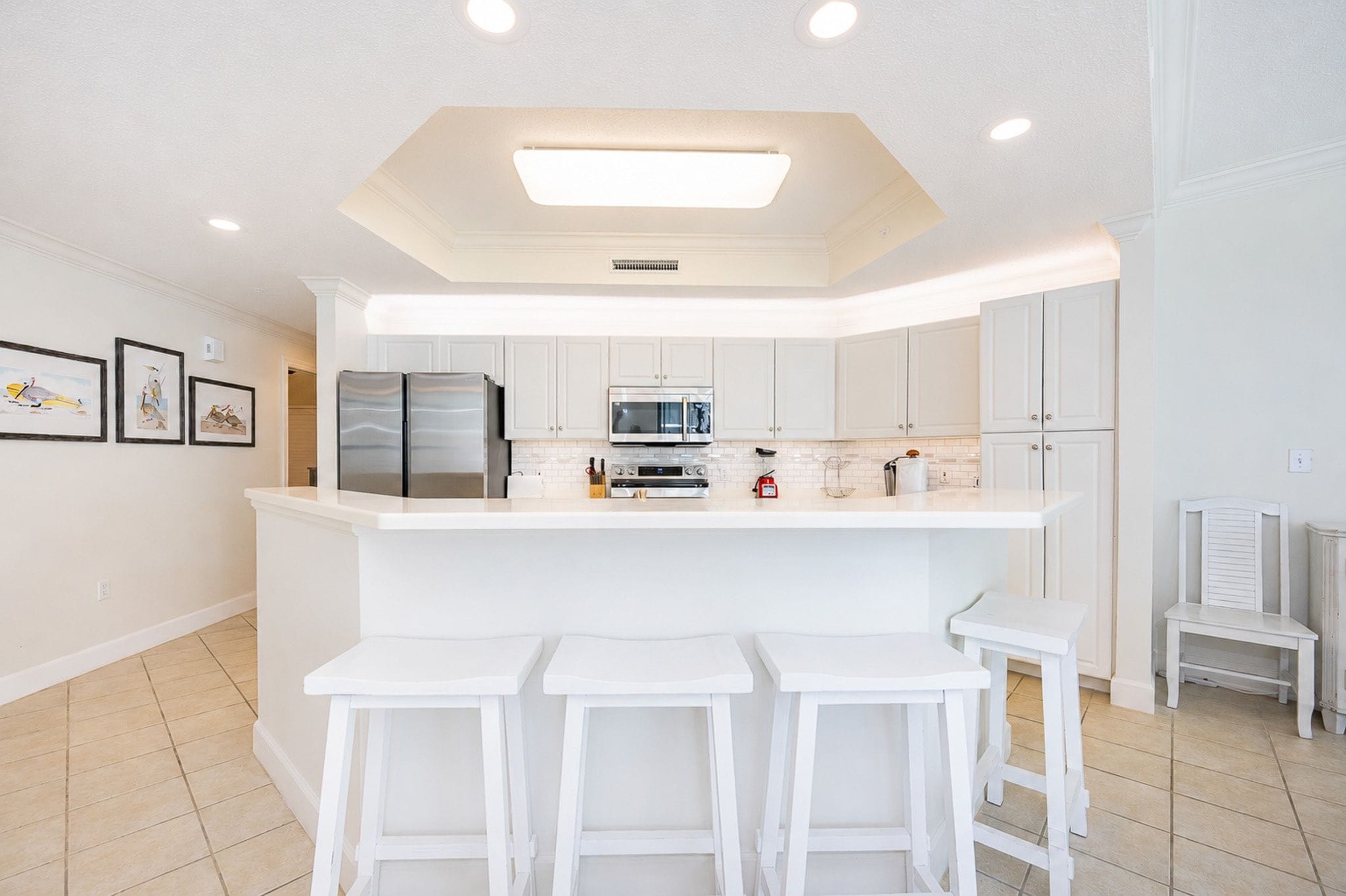 Una cocina moderna con armarios blancos, una isla central con taburetes y horno integrado, además de un microondas.