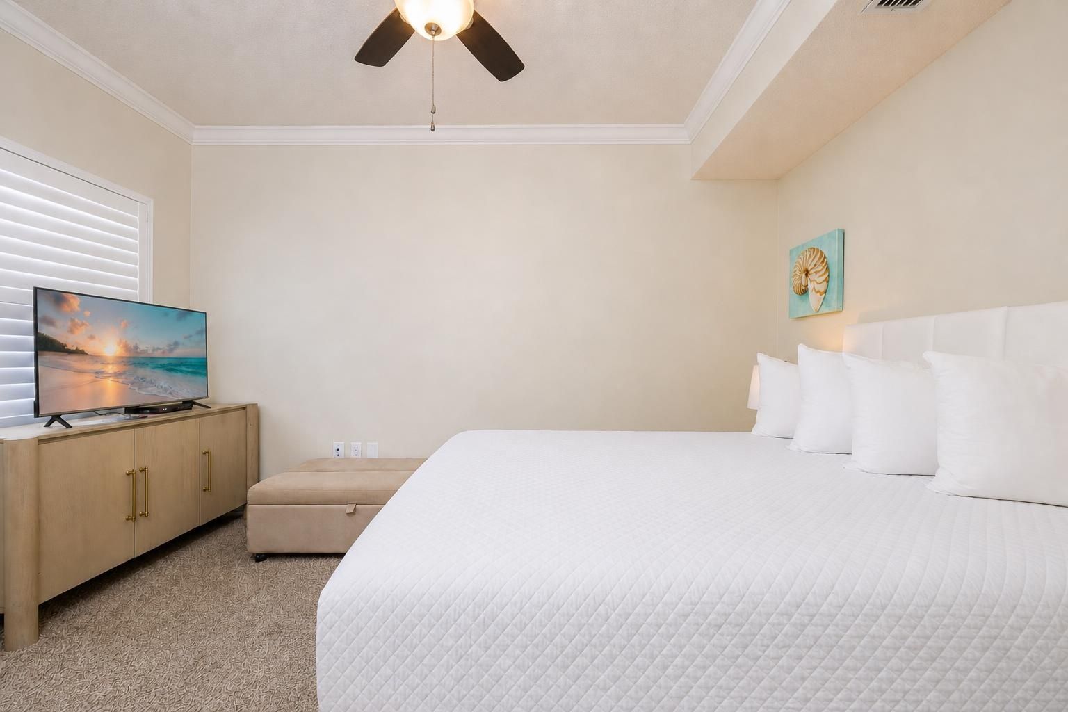 Une chambre d’hôtel avec un lit, un téléviseur posé sur une commode en bois, un ventilateur de plafond et un tableau accroché au mur.