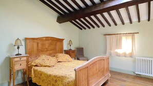 Een slaapkamer met een houten bed, twee nachtkastjes met lampen, een raam met gordijnen en een radiator.