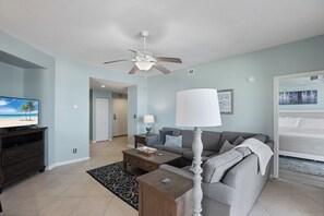 A living room with a ceiling fan, a television, a sofa, a coffee table, and a lamp. - Beautiful 3 bedroom/ 3 bath condo located on the 5th floor in East tower (ORANGE BEACH)