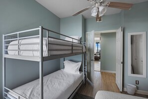 A bunk bed room with a ceiling fan, a door leading to another room, and a white trash bin. - Beautiful 3 bedroom/ 3 bath condo located on the 5th floor in East tower (ORANGE BEACH)