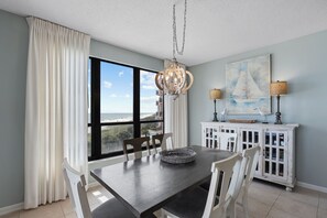 A dining area with a view of the beach, a chandelier, and a nautical-themed painting. - Beautiful 3 bedroom/ 3 bath condo located on the 5th floor in East tower (ORANGE BEACH)