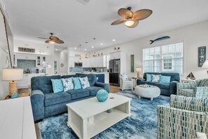 A modern living room with a blue sofa, white coffee table, and a dining area with a kitchen in the background. - Blue Star Oasis by Duncan Real Estate (Holmes Beach)