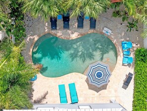 Vue aérienne d’une piscine avec des chaises longues et un parasol.