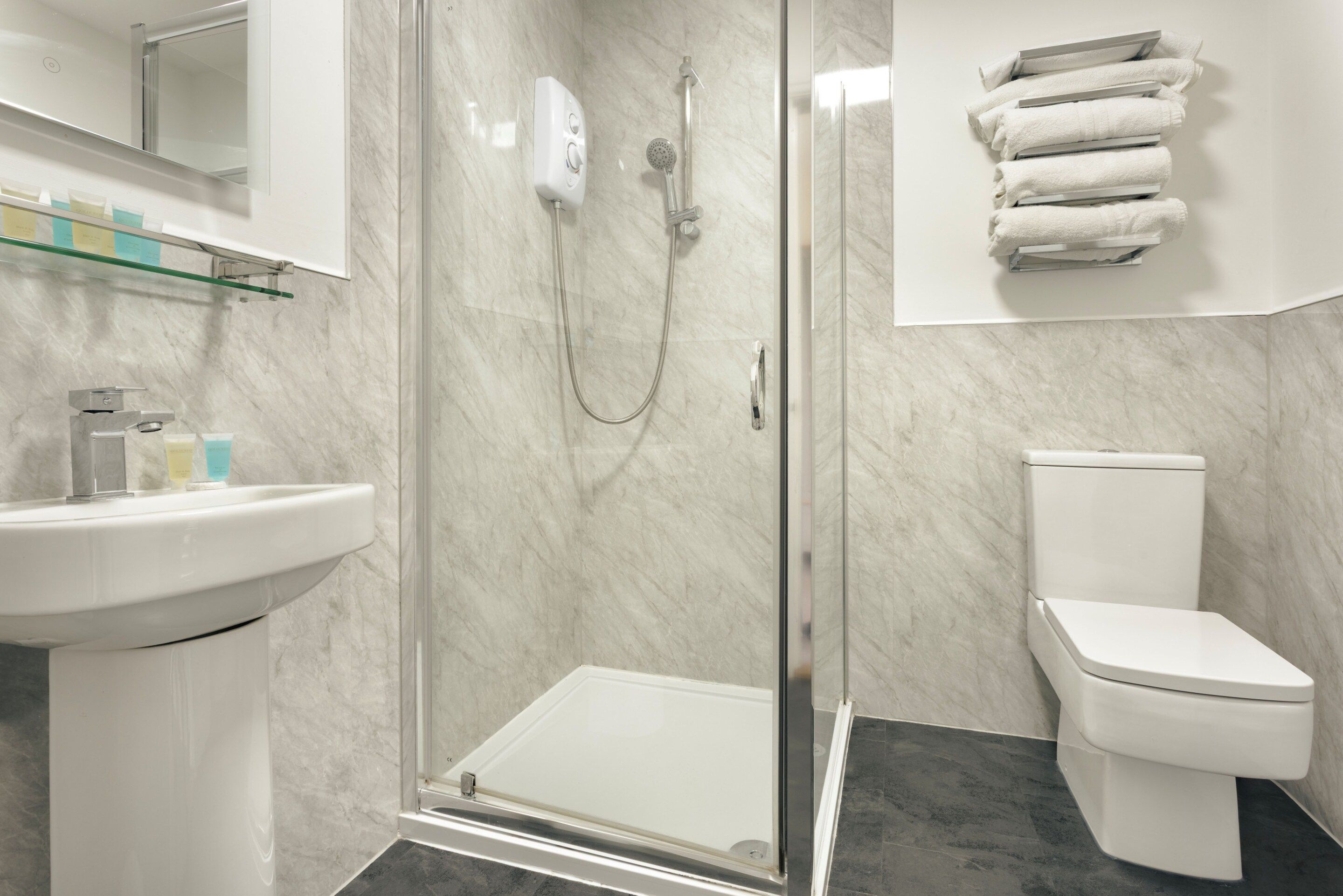A modern bathroom with a glass-enclosed shower, a white toilet, and a sink with a marble countertop.