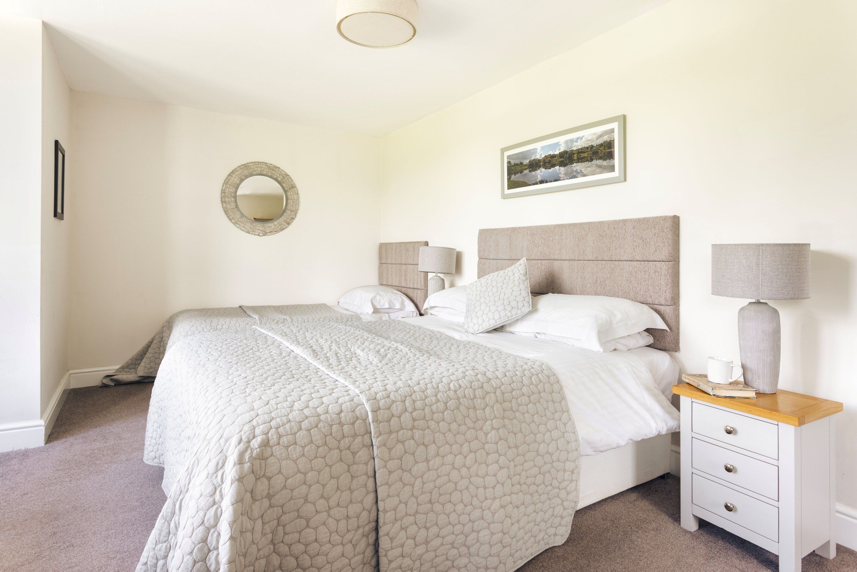 A neatly arranged bedroom with a large bed, bedside tables, a mirror, and a framed picture on the wall.