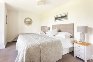 Ein ordentlich eingerichtetes Schlafzimmer mit einem großen Bett, Nachttischen, einem Spiegel und einem gerahmten Bild an der Wand.