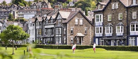 Un campo de golf con jugadores, rodeado de casas tradicionales de piedra y madera con múltiples ventanas y balcones.