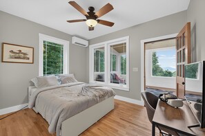 A bedroom with a bed, a desk, and a chair. There are windows and a ceiling fan. - Peaceful Cozy Cabin Expansive Views & Sunroom (Waynesville)